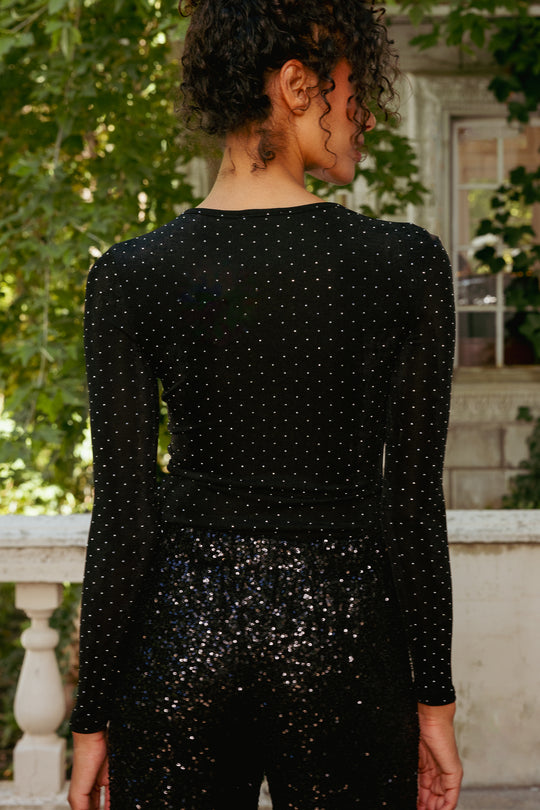 Person wearing a black sequin dress standing outdoors with greenery in the background