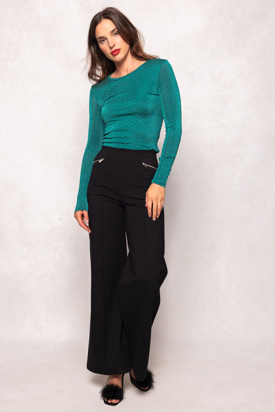 A woman poses against a light background, wearing the maternity-friendly Bravo Top in Emerald by Ivy City Co, paired with black wide-leg pants and open-toed black shoes featuring fur accents.