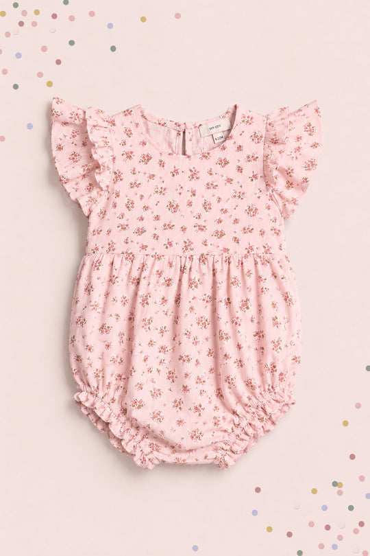 Mark her special milestones with the Ivy City Co Baby Hattie Romper in Madeline Pink—a sweet pink baby romper adorned with short ruffled sleeves and a delicate small floral print. Ideal for first birthday photos, it’s showcased on a light pink backdrop sprinkled with pastel confetti for an added dose of charm.