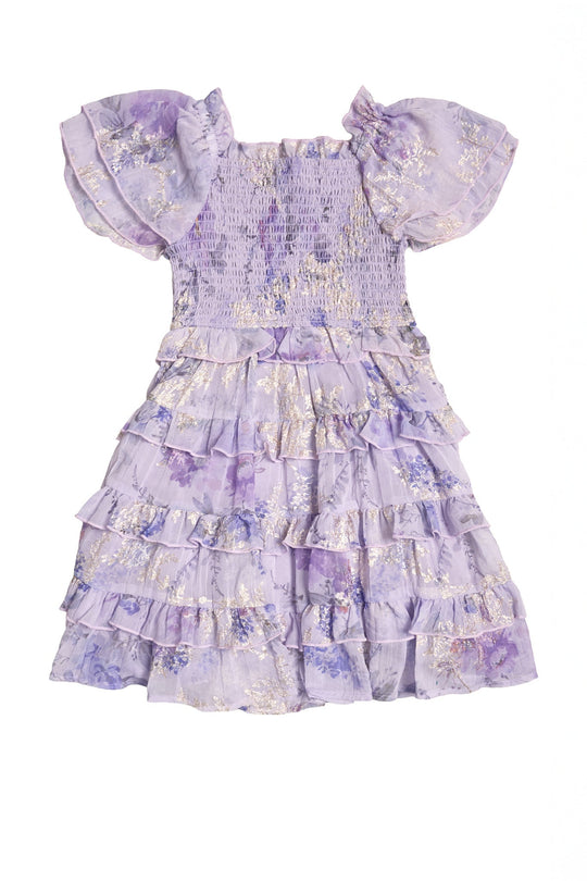 The Mini Winnie Dress in Lavender Aquarelle Fleur by Ivy City Co is a girls’ spring dress adorned with floral patterns, delicate gold accents, and short puff sleeves. This enchanting piece features a smocked bodice and a layered ruffle skirt, creating a festive and charming look.