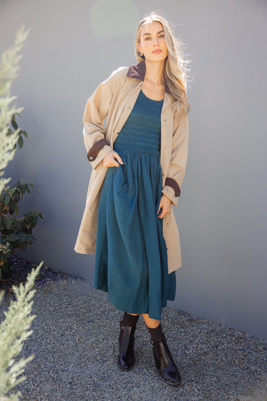 Woman wearing a teal dress and beige cardigan against a gray wall.
