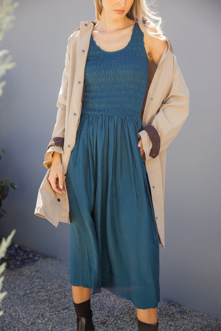 Woman wearing a blue dress and beige coat against a gray background