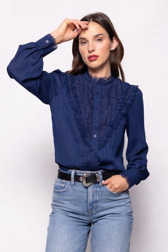 A woman is wearing the Ivy City Co Blythe Blouse in Navy, a long-sleeve, button-down top paired with light blue jeans. She stands against a white background with one hand touching her forehead. This elegant blouse is nursing-friendly, combining style and convenience.