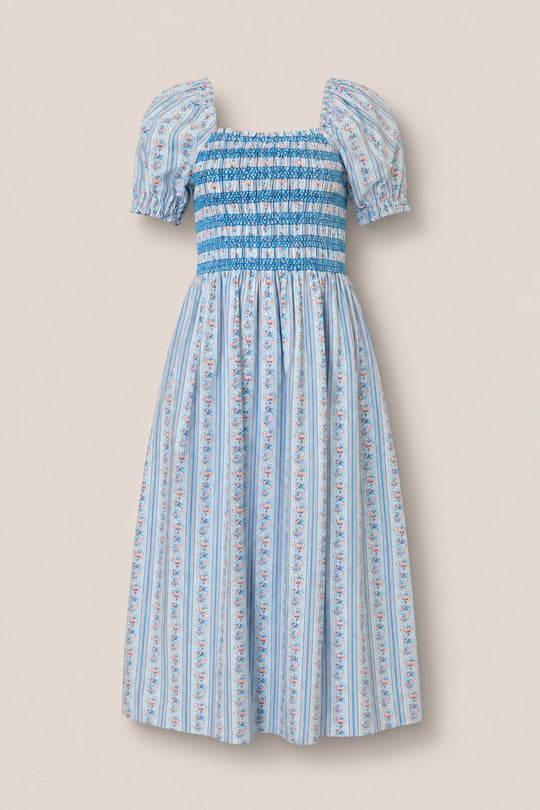 The Sunday Best Dress in Rosette Linear Stripe by Ivy City Co is a light blue cotton midi dress featuring puffed short sleeves, a smocked bodice, and a flared skirt. Designed with vertical floral and stripe patterns in shades of blue, pink, and white, this breezy summer style is also maternity friendly.