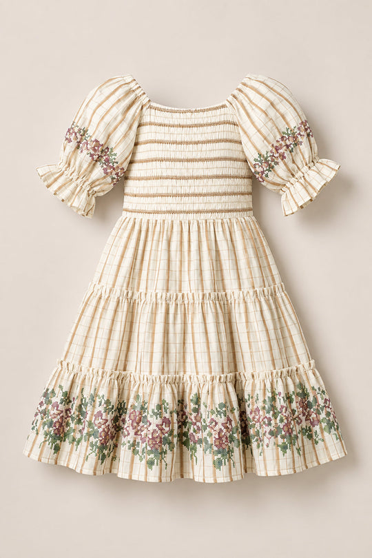 The Mini Madeline Dress in Embroidered Cider Grid by Ivy City Co is cream-colored with a charming checkered pattern, featuring short puff sleeves, a smocked bodice, and a tiered skirt. Delicate floral embroidery accents the sleeves and hem. The dress is displayed laid flat on a neutral background.