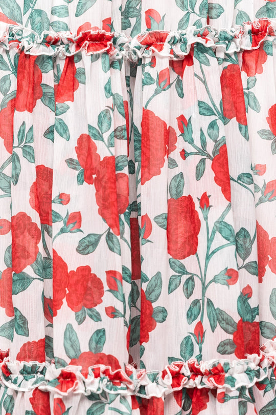 A close-up of white fabric adorned with a red and green rose pattern and ruffled horizontal seams, featured in the Ivy City Co Selena Dress in Red Roses—a chiffon midi style that’s also maternity friendly.