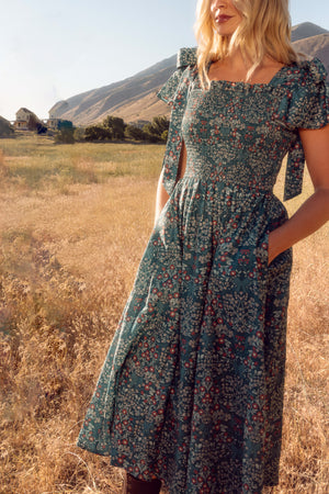 Woman in a floral dress standing in a field with mountains in the background