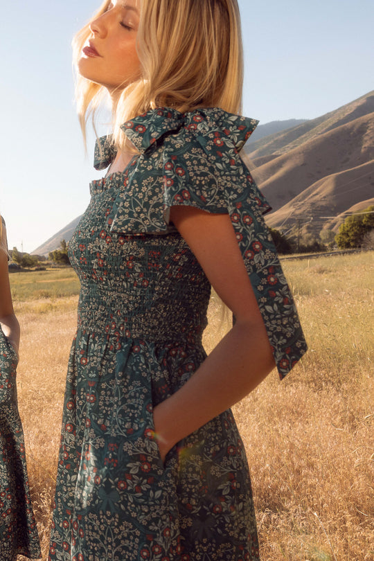 Woman in a floral dress standing in a field with mountains in the background