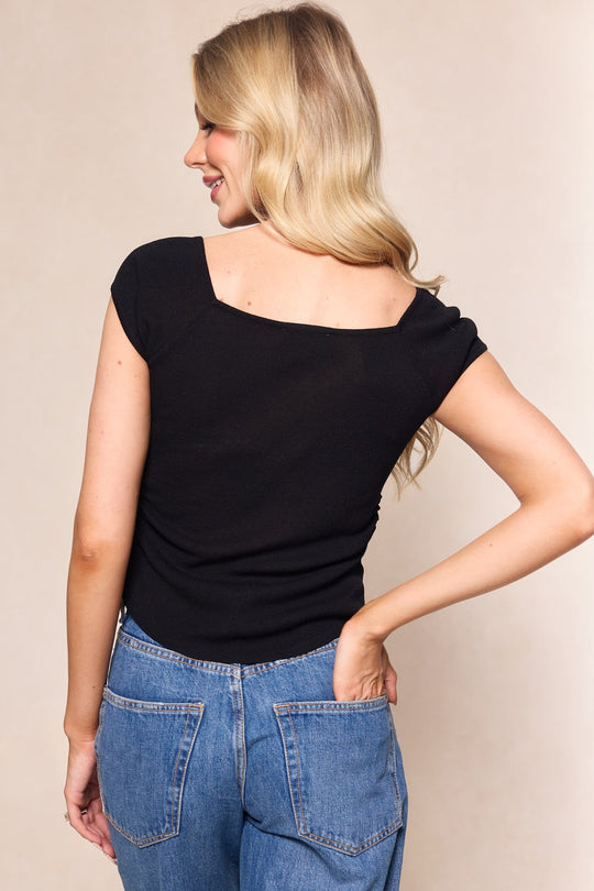 Wearing the Aspen Shirt in Black by Ivy City Co, a woman with long blonde hair and blue jeans stands facing away, one hand in her back pocket and the other on her hip, smiling over her shoulder.