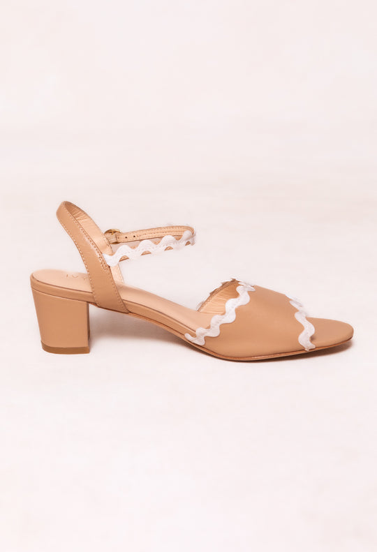 The Lois Heel in Tan by Ivy City Co is a tan leather shoe with an open toe and medium block heel, featuring white ric rac trim on the adjustable ankle and toe straps, displayed against a plain light background.