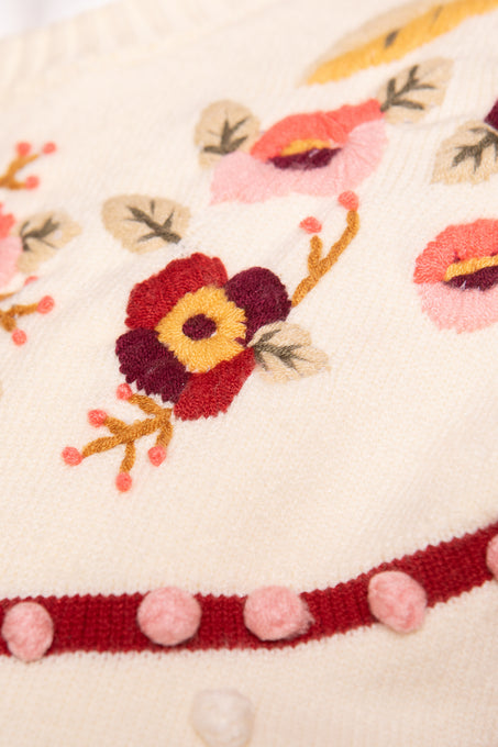 Close-up of the Sylvie Sweater in Cream by Ivy City Co—features red, pink, yellow, and purple floral embroidery, a red border, and pink yarn accents; designed as a maternity-friendly option.