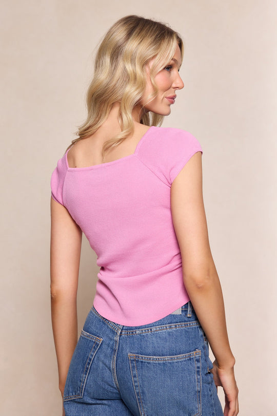 Wearing the Ivy City Co Aspen Shirt in Pink paired with blue jeans, a woman with wavy blonde hair stands against a plain light background, her head turned to the side—an effortlessly stylish look perfect for any spring wardrobe.