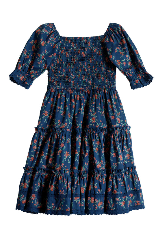 The Mini Madeline Dress in Midnight Vibrant Chintz by Ivy City Co is a girls’ midi dress featuring a vibrant blue floral chintz pattern, short puff sleeves with ruffle details, a smocked bodice, and a tiered skirt—perfect for any occasion.