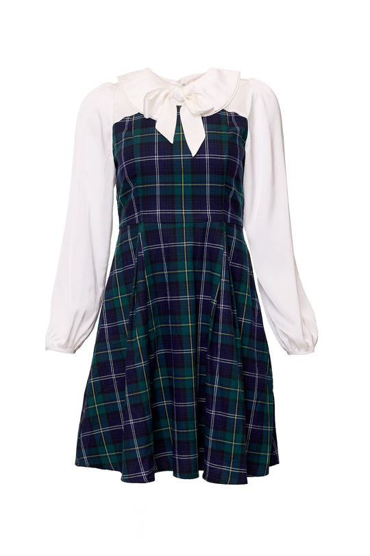 The Tawny Dress in Nocturne Plaid by Ivy City Co features a green and navy plaid skirt and bodice, white long sleeves, a white collar, and a large white bow at the neckline.