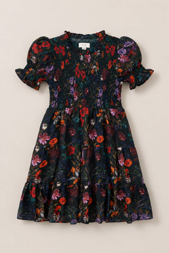 The Mini Cordelia Dress in Evergreen Vivid Meadow by Ivy City Co is a short-sleeved, knee-length floral dress for girls, designed with puff sleeves, a smocked bodice, and a ruffled collar, showcasing vibrant red, purple, and green flower patterns on a dark background.