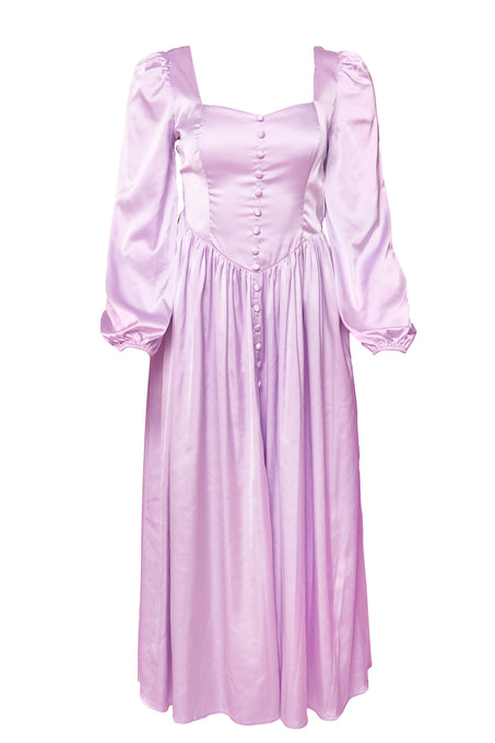 The Valentina Dress in Lavender by Ivy City Co is a light purple satin dress with long puff sleeves, a fitted bodice, front buttons, vintage-inspired gathered skirt, and a charming lace-up corset back.