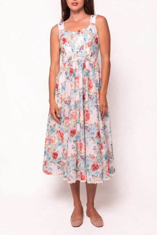 A woman stands against a white background with her arms relaxed at her sides, wearing the Ivy City Co Penny Tank Midi Dress in Multicolor Floral. The sleeveless, cotton eyelet dress features a fitted bodice and flared, ankle-length skirt. She completes the look with light pink flat shoes.