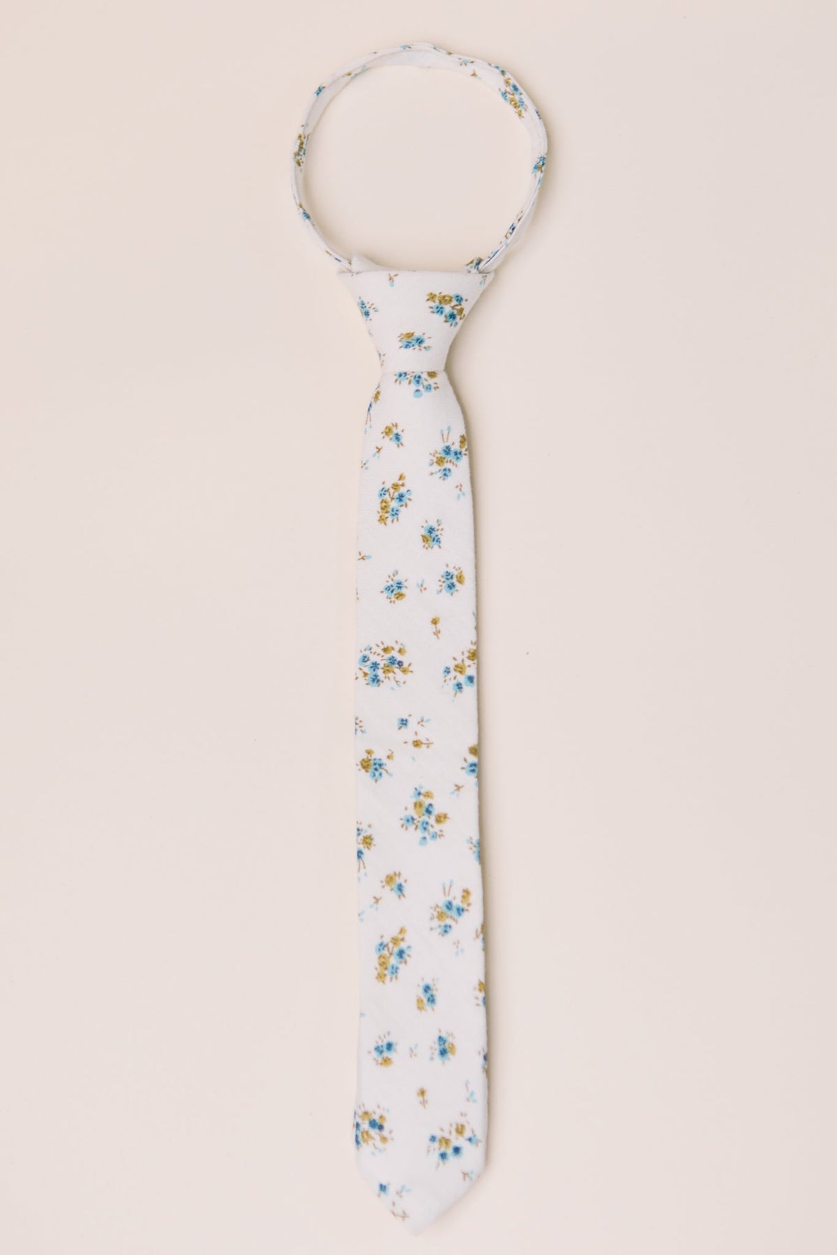 A white necktie featuring a delicate blue and yellow floral pattern from Ivy City Co’s Ties in Madeline Blue Floral collection, displayed on a subtle light background—an ideal option for those seeking coordinating family matching accessories.