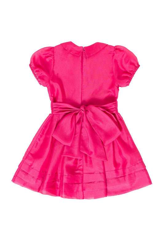 The Mini Cassian Dress in Hot Pink by Ivy City Co features a bright, fitted waist, large back bow, pleated skirt, and decorative collar. Displayed on a white background, this girls’ party dress is perfect for special occasions.