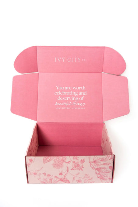 An open Ivy City Co Gift Box in pink with a floral pattern reveals the message inside: You are worth celebrating and deserving of beautiful things.