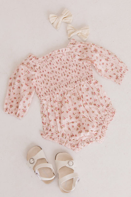 The Ivy City Co Baby Madeline Romper in Pink, paired with cream hair bows and white sandals, is arranged on a light surface—an adorable puff sleeve set perfect for your little one.