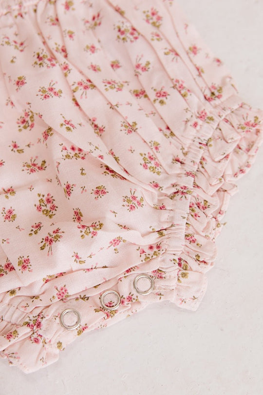 The Ivy City Co Baby Madeline Romper in Pink features a small floral print, ruffled edges, and metal snap buttons—perfect for pairing with your favorite bloomers or wearing on its own.